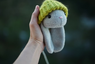 Hand holding a crocheted bunny with a green hat
