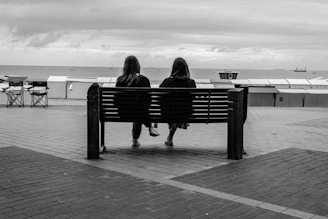 Two people sit on a bench overlooking the ocean.