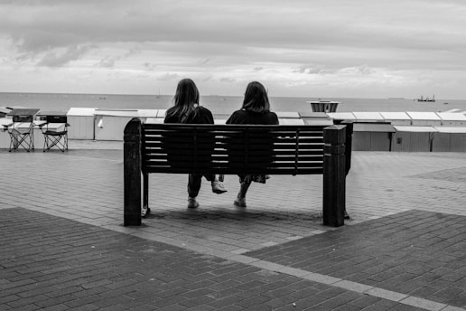 Two people sit on a bench overlooking the ocean.