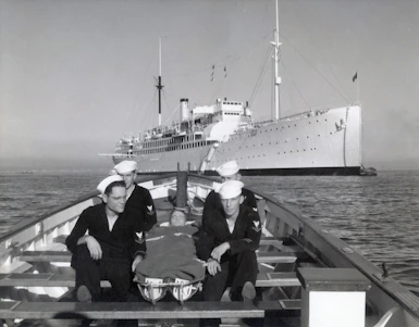 Sailors in a boat with a ship behind them.