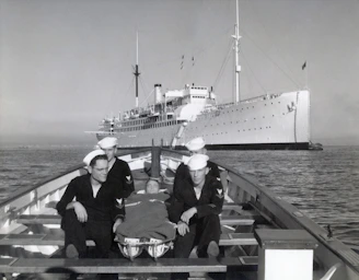 Sailors in a boat with a ship behind them.