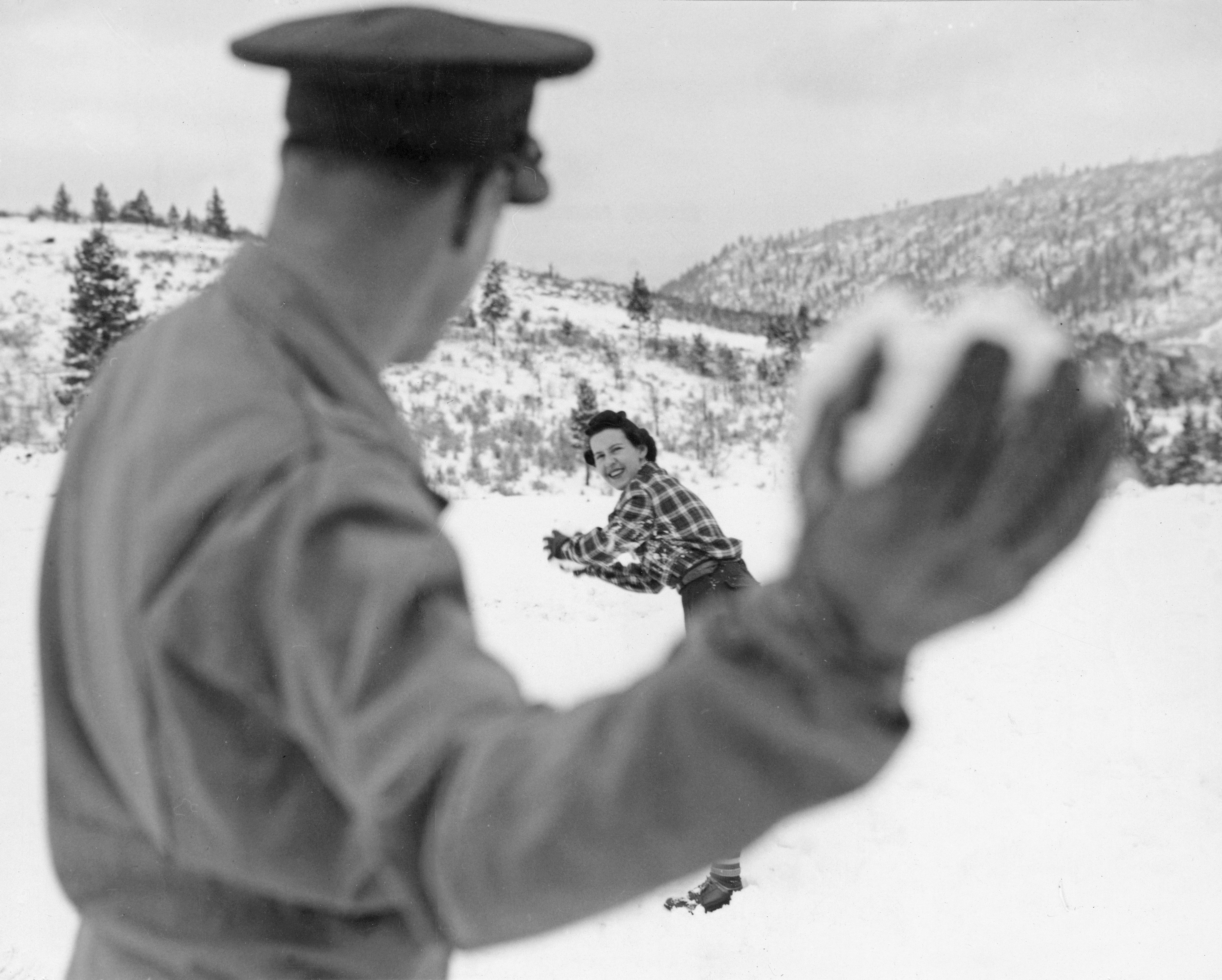 Uomo che lancia una palla di neve contro una donna in un paesaggio innevato