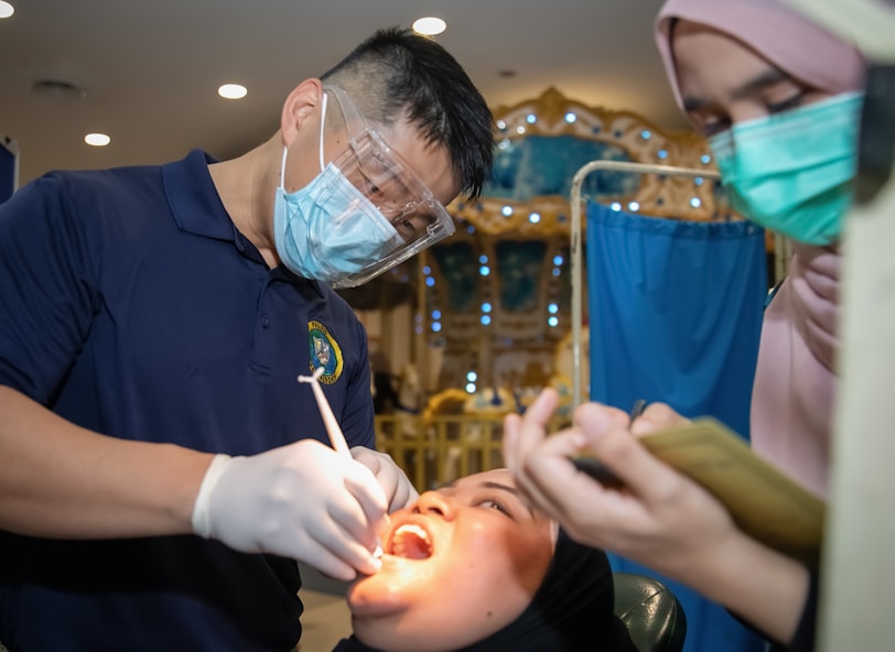 Dentist examining patient's teeth with assistant nearby.