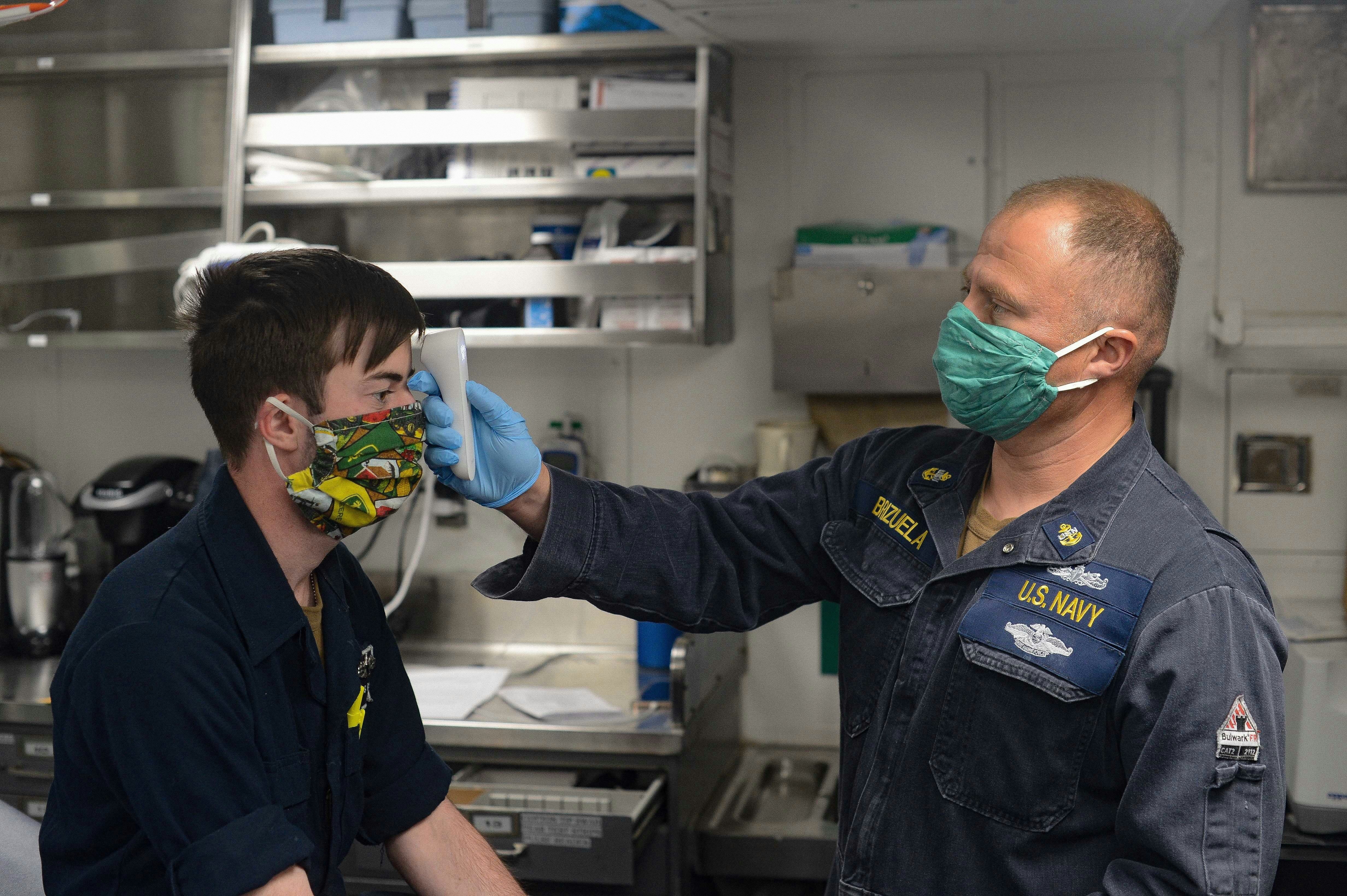 Navy officer checks sailor's temperature with thermometer.