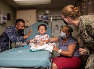 A child sits on a medical bed with adults around.