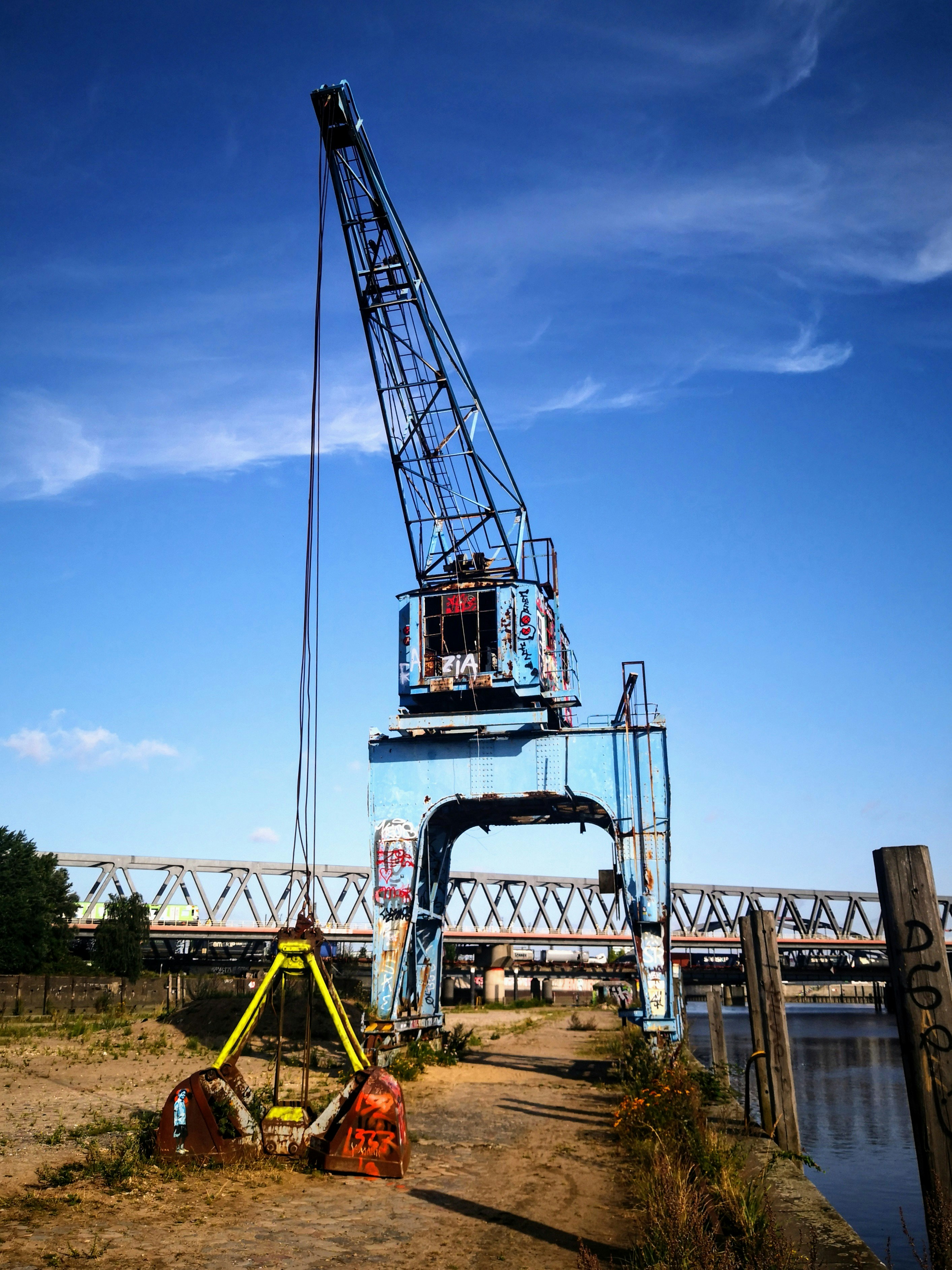 An old blue industrial crane stands by the water.