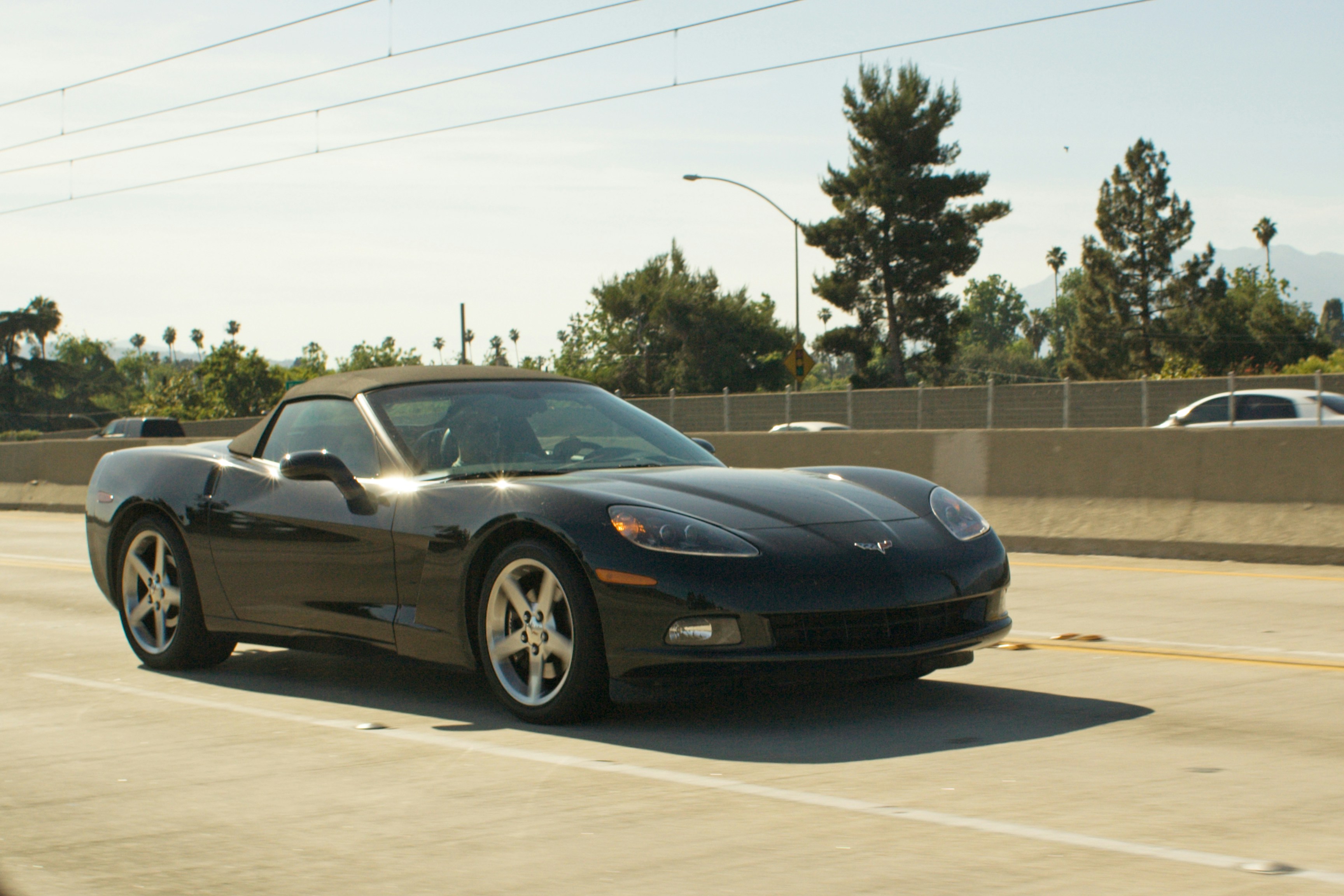 A black convertible corvette drives on a sunny highway.