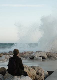 Man watches large waves crash on rocky shore.