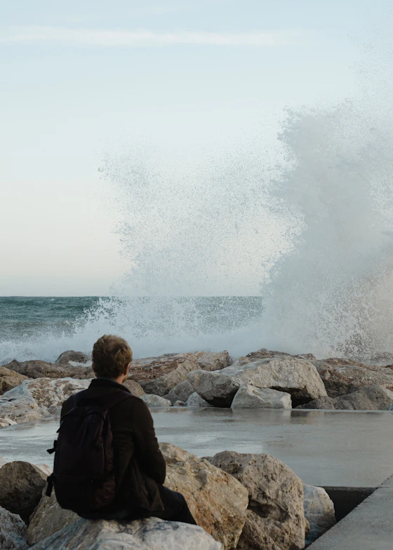 Man watches large waves crash on rocky shore.