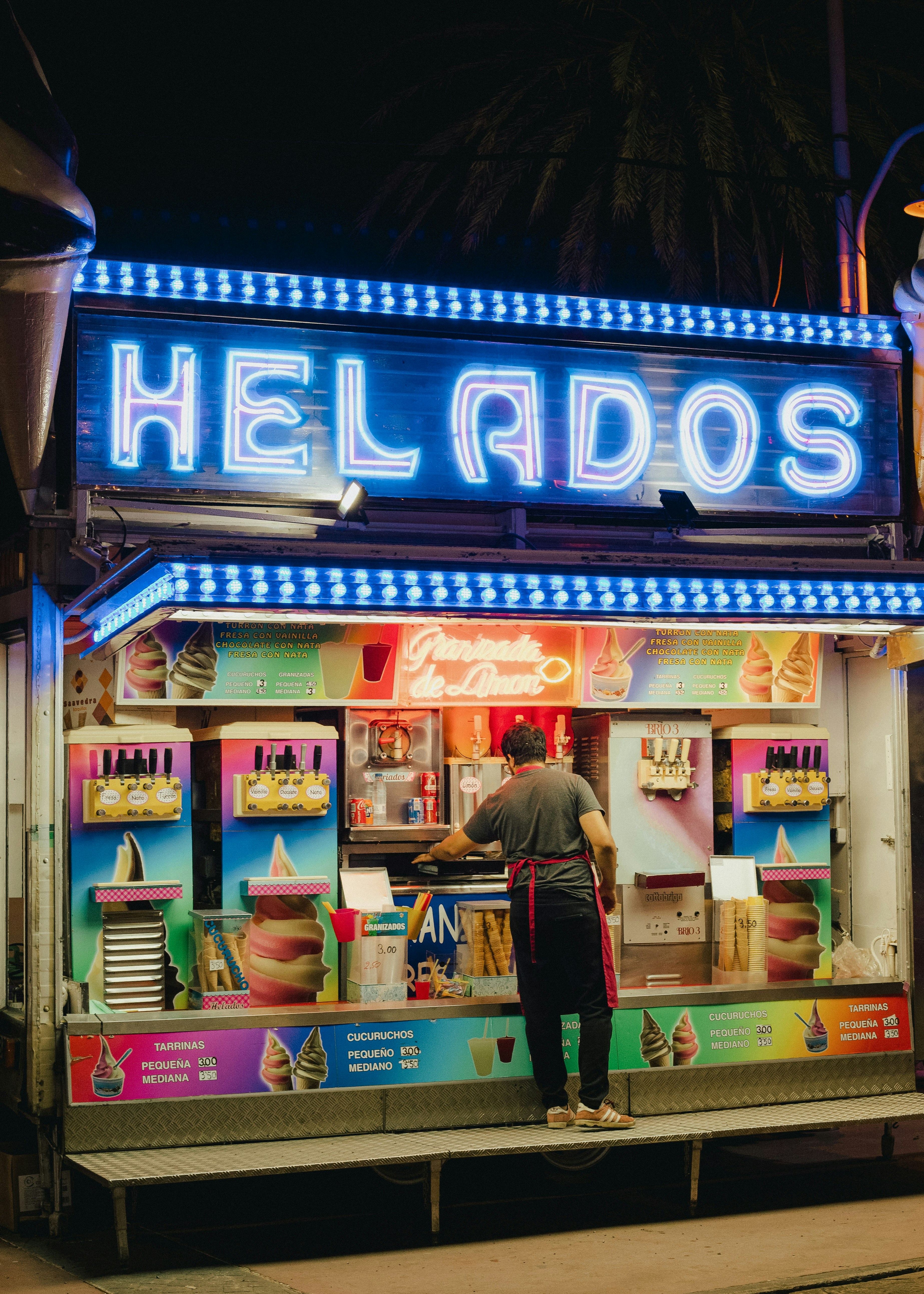 Person serving ice cream at a brightly lit stand.