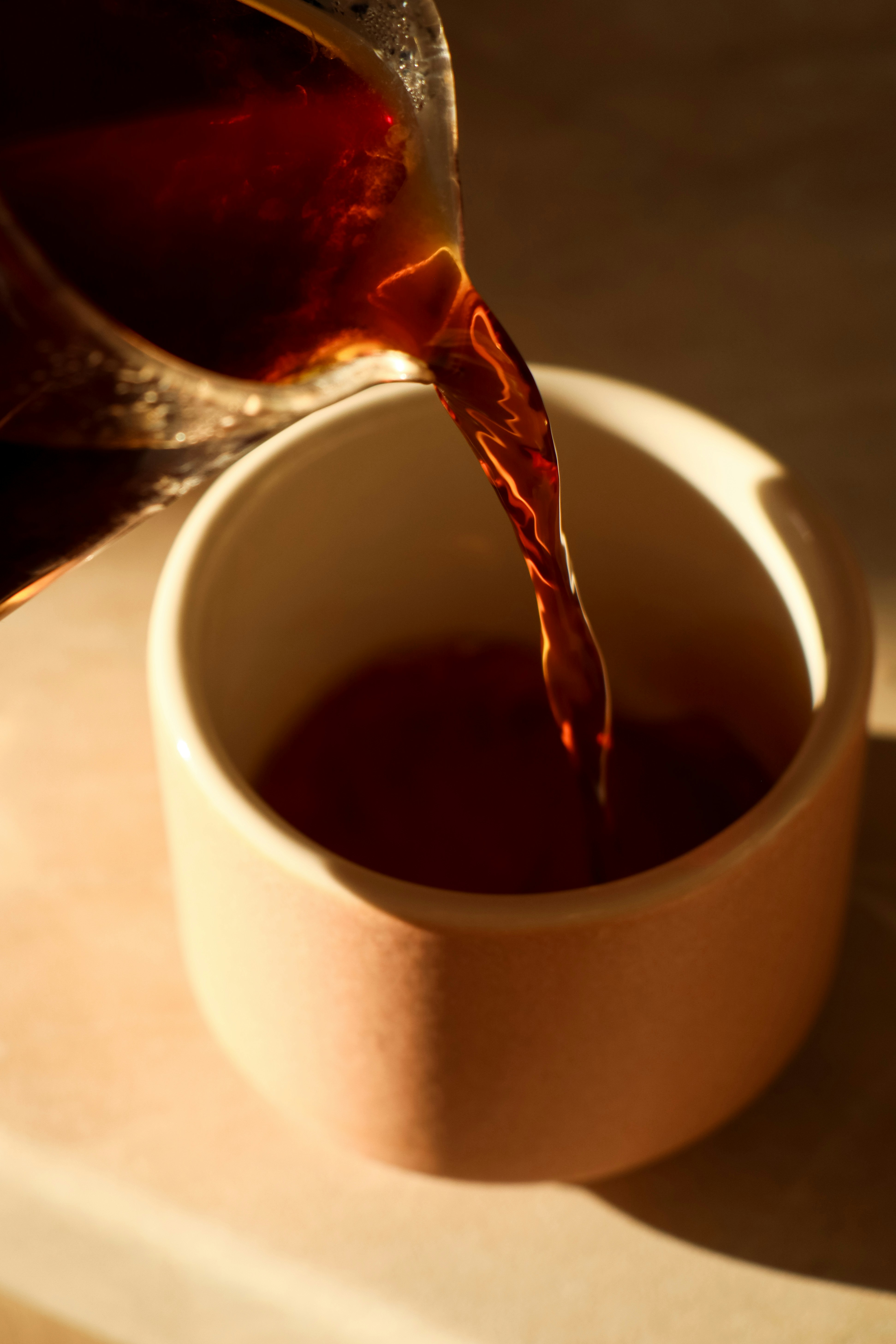 Dark coffee being poured into a light pink cup.