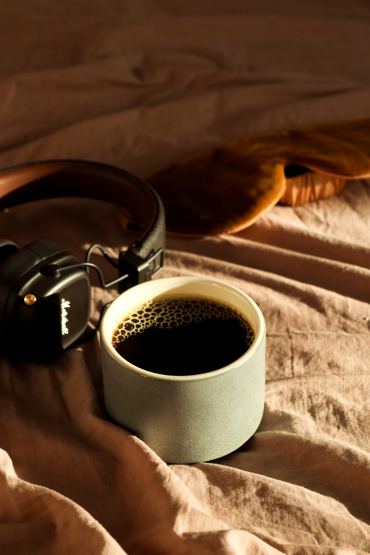 Coffee and headphones on an unmade bed