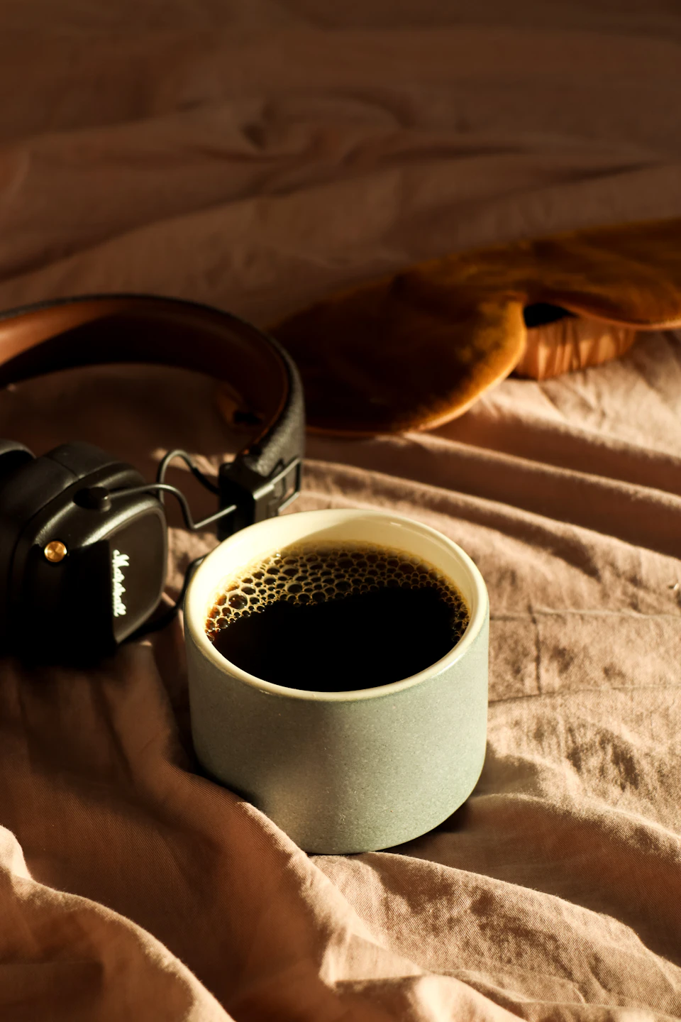 Coffee and headphones on an unmade bed