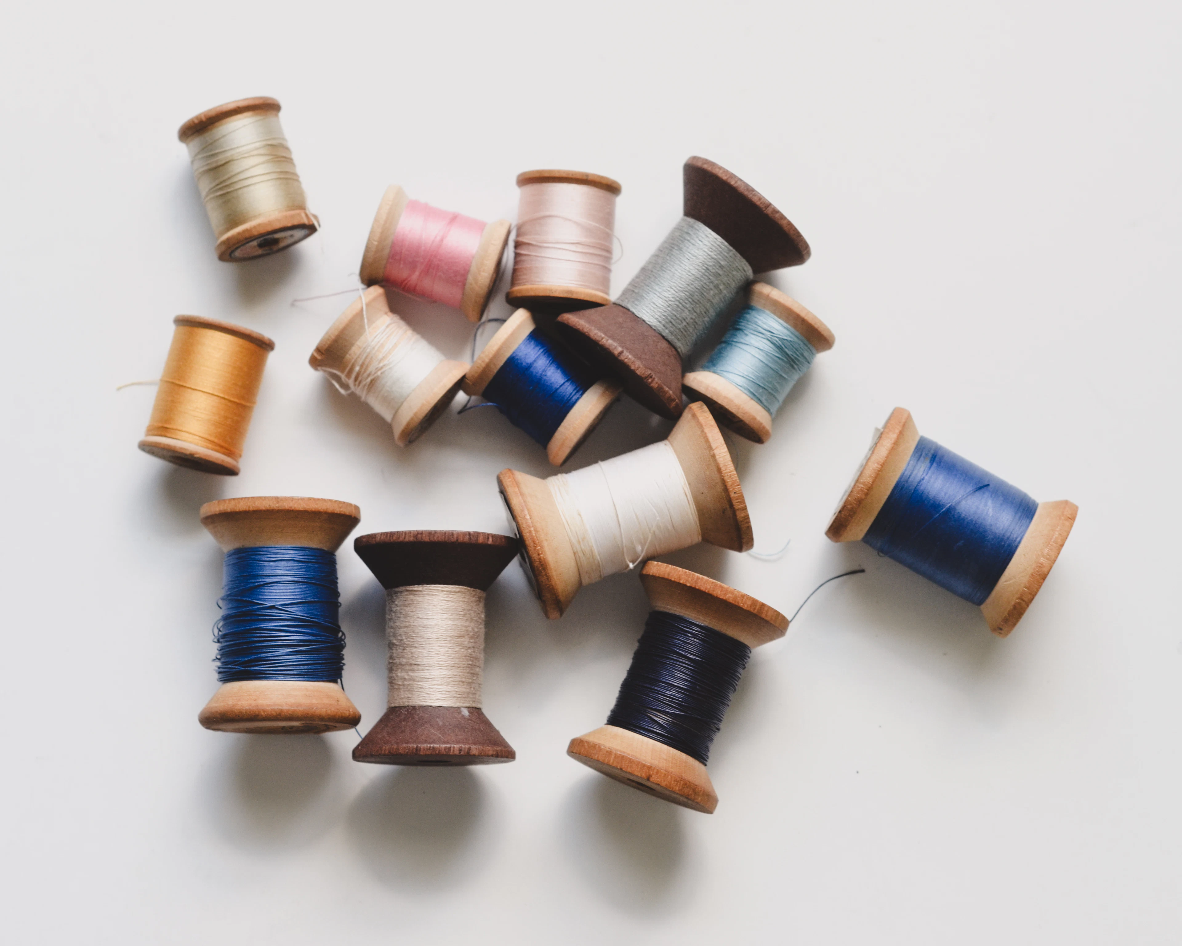 Wooden spools of thread in blues, creams and pinks scattered on a white surface.