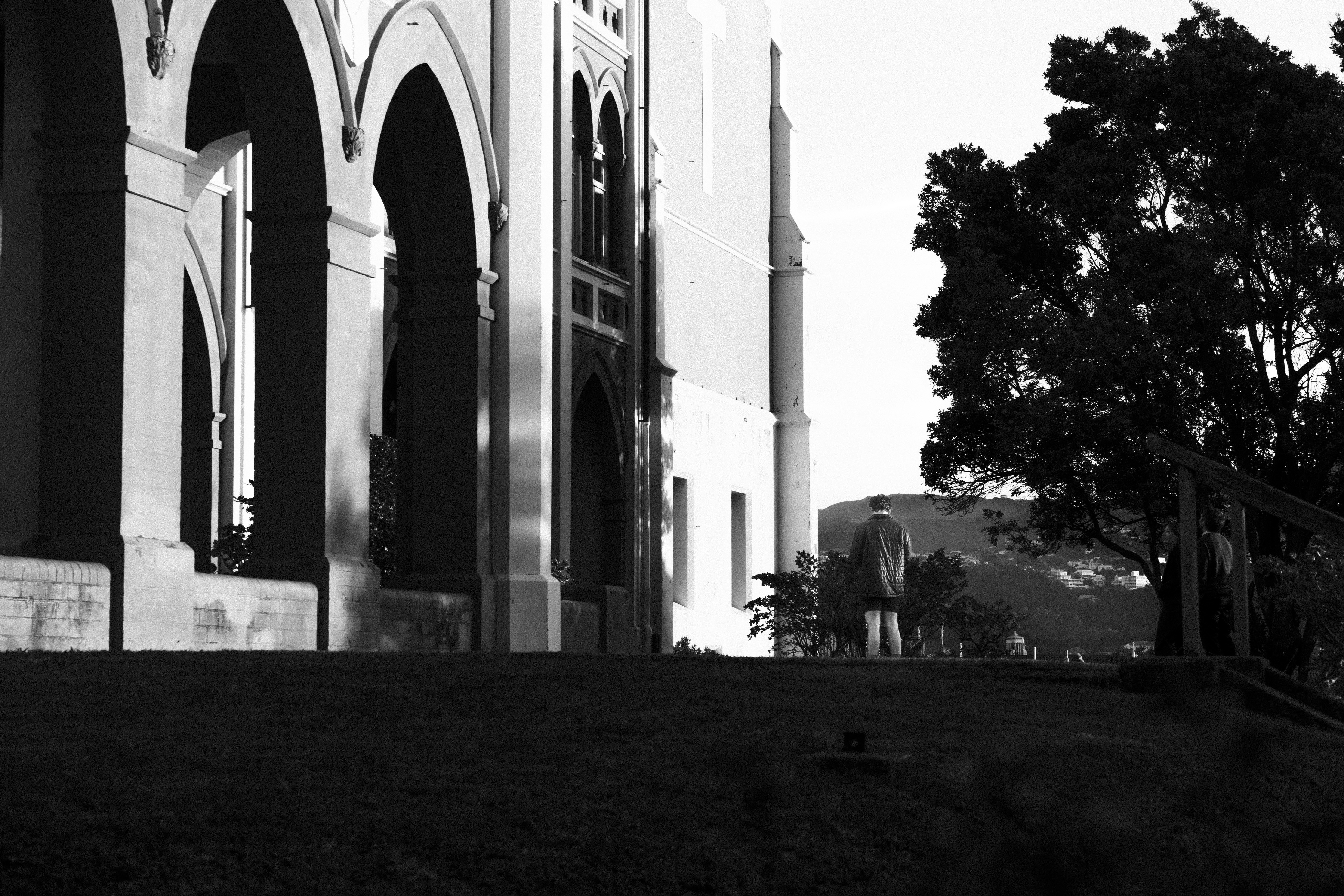 People walk near a large building with arches.