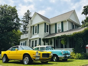 Two vintage cars parked in front of a large house.