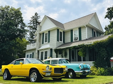 Two vintage cars parked in front of a large house.