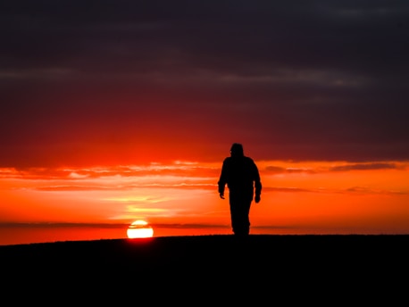 Silhouette of a person walking towards the sunset.