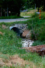 Creek flows through culvert under a rural road.