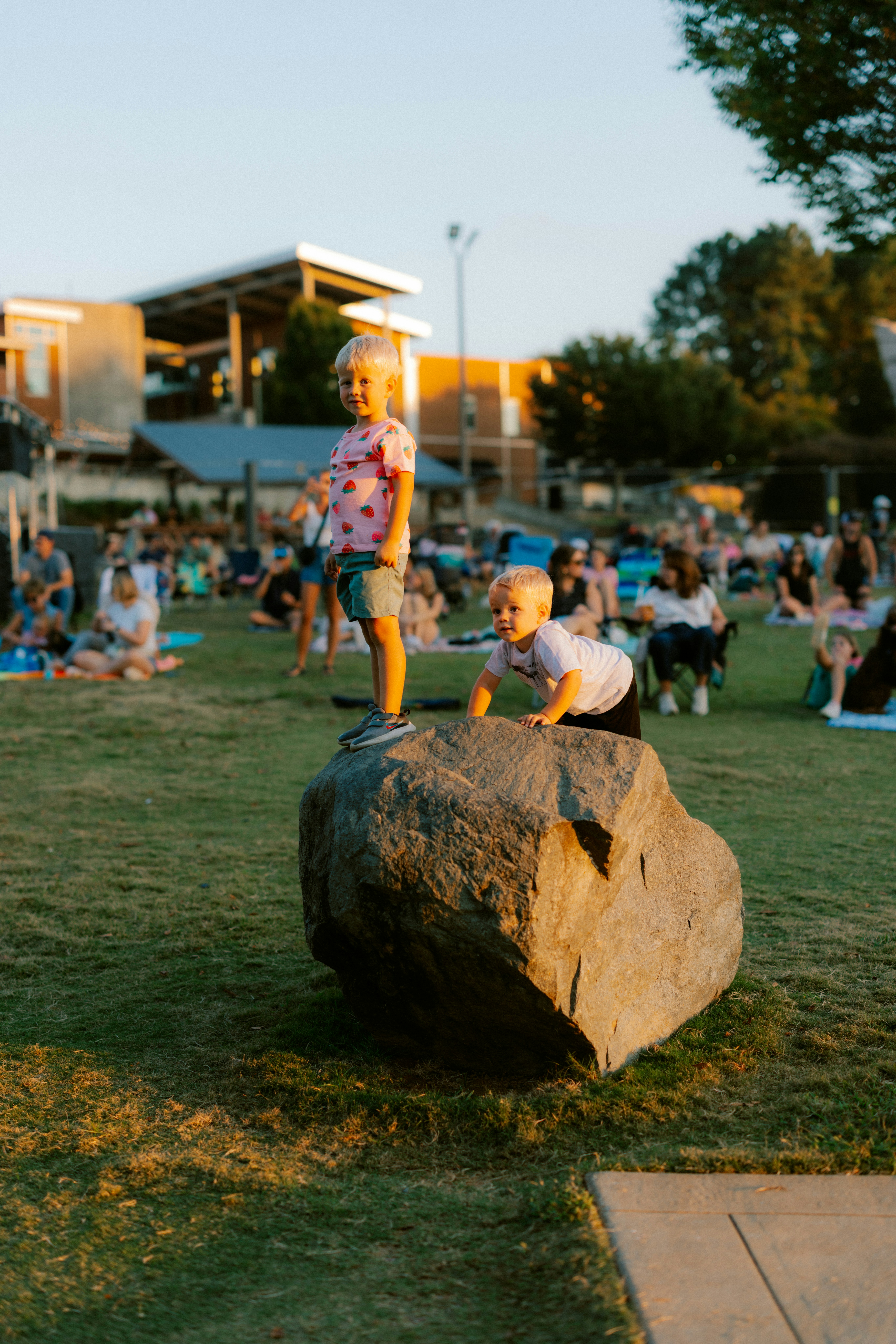 Two young children playing on a large rock outdoors.