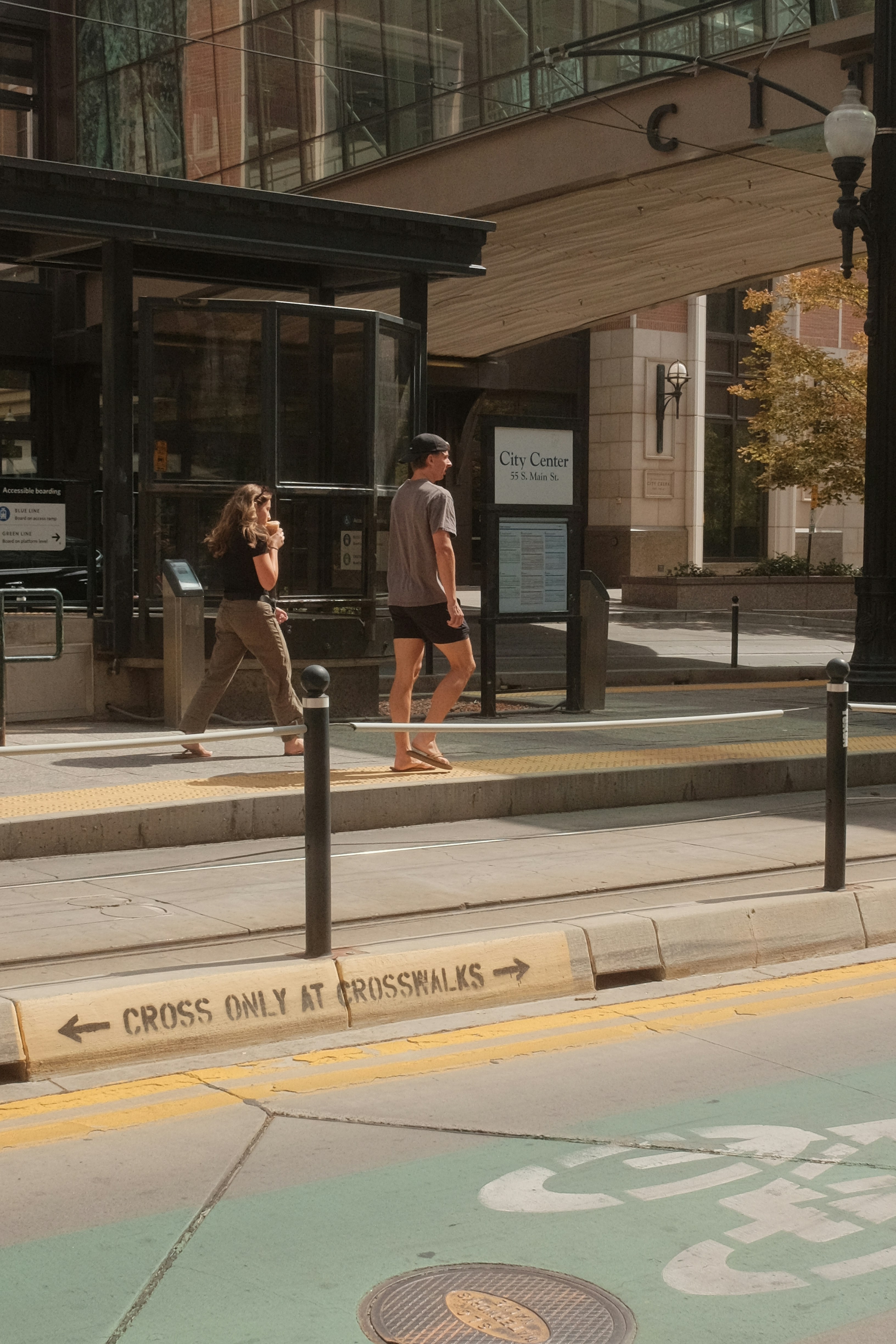 Two people walk across a crosswalk near a bus stop.