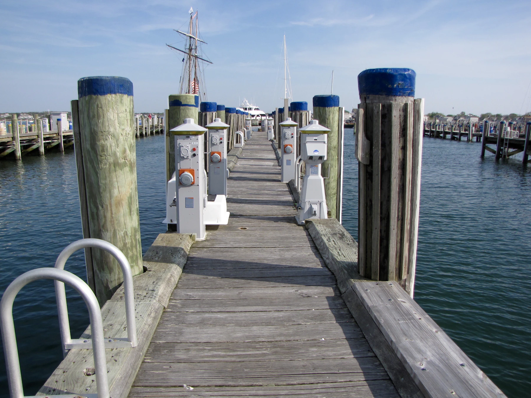 A long wooden pier with blue-capped posts leading out between moored boats