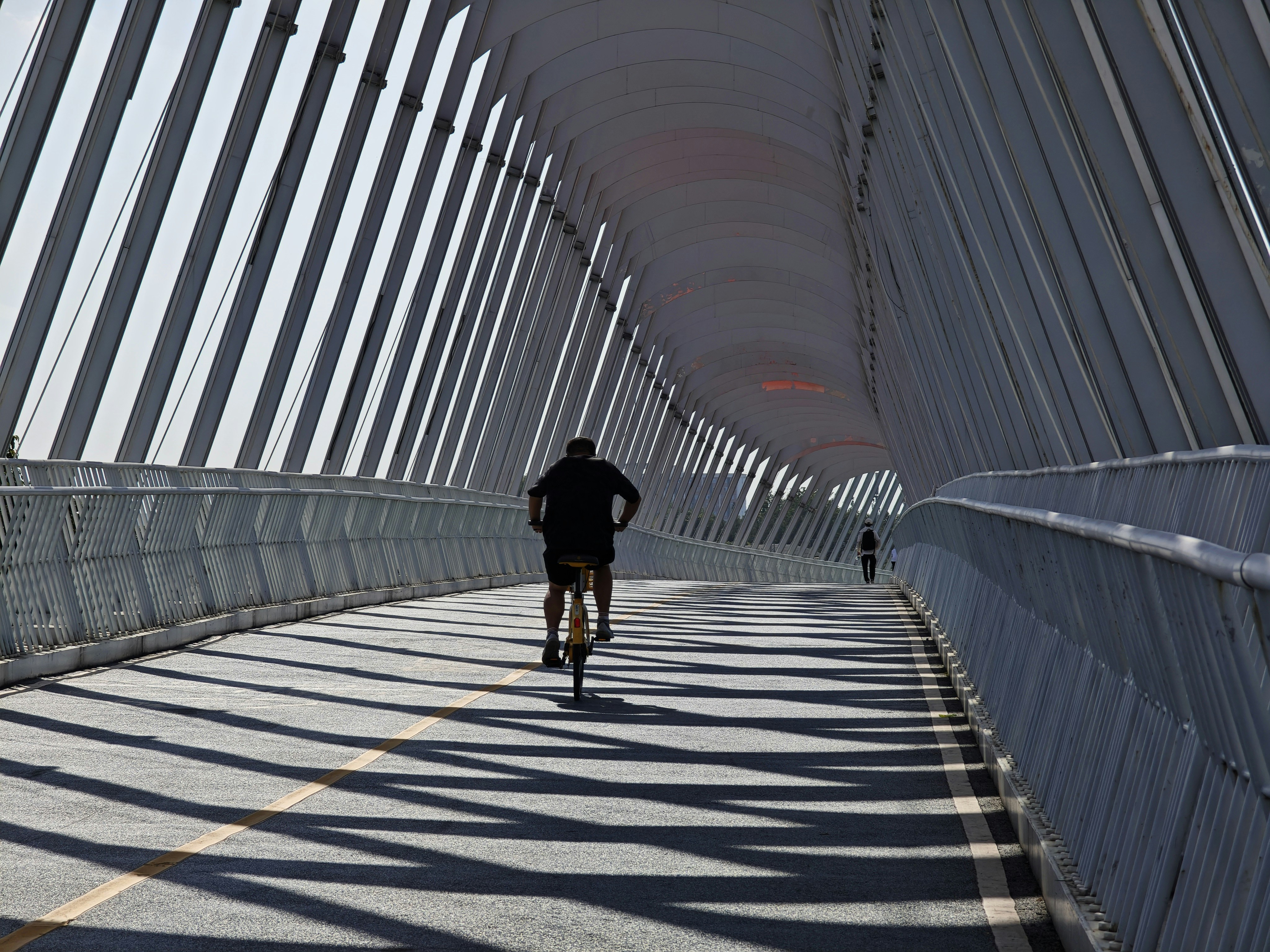Cyclist on a modern bridge with striking shadow patterns.
