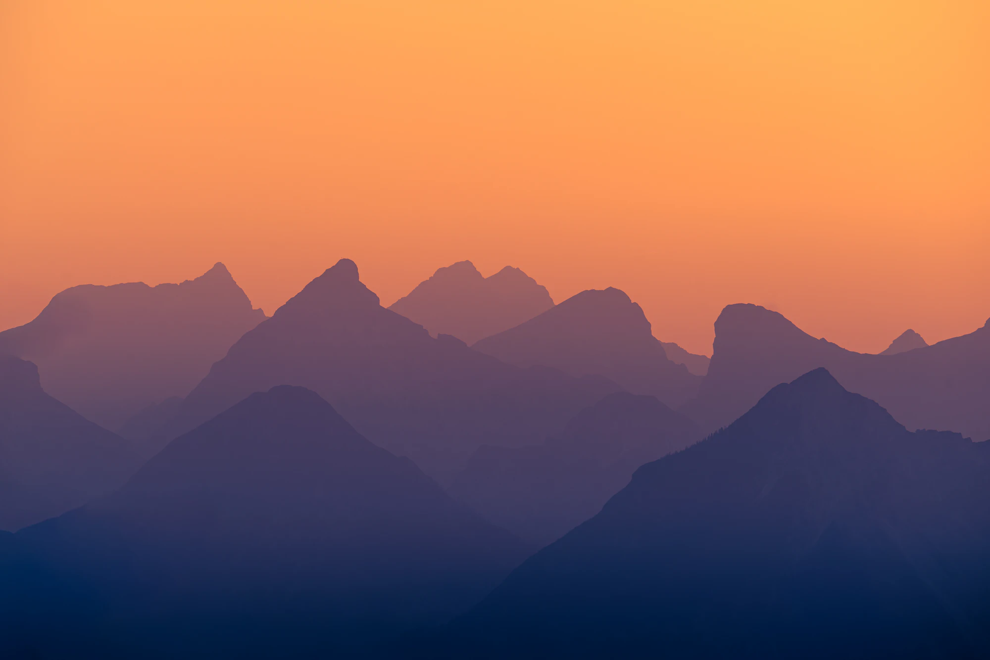 Layered mountain peaks at sunset with orange sky