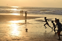 Children play soccer on a beach at sunset