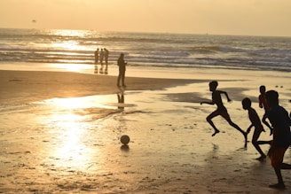 Children play soccer on a beach at sunset