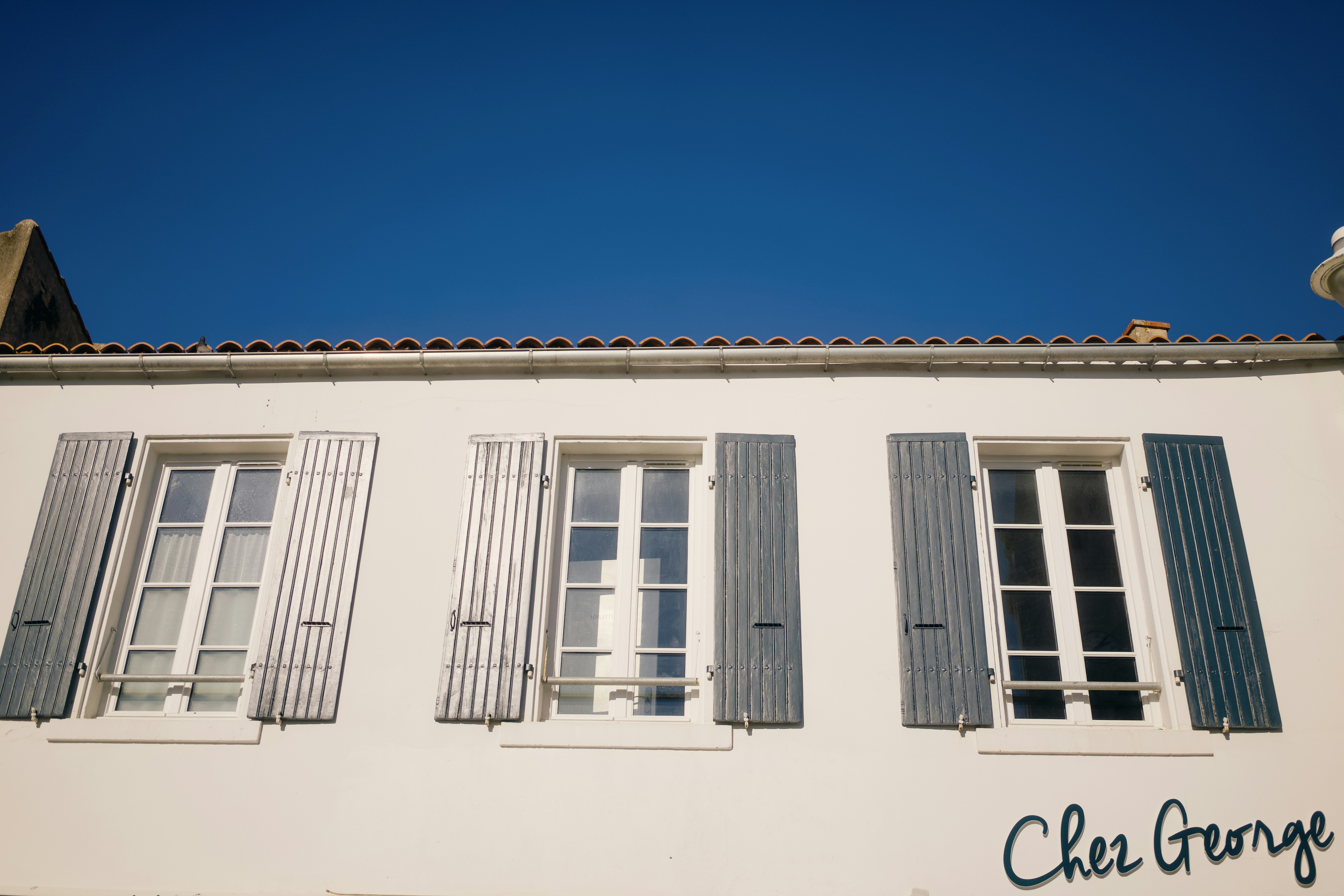 White building facade with three windows and blue sky.