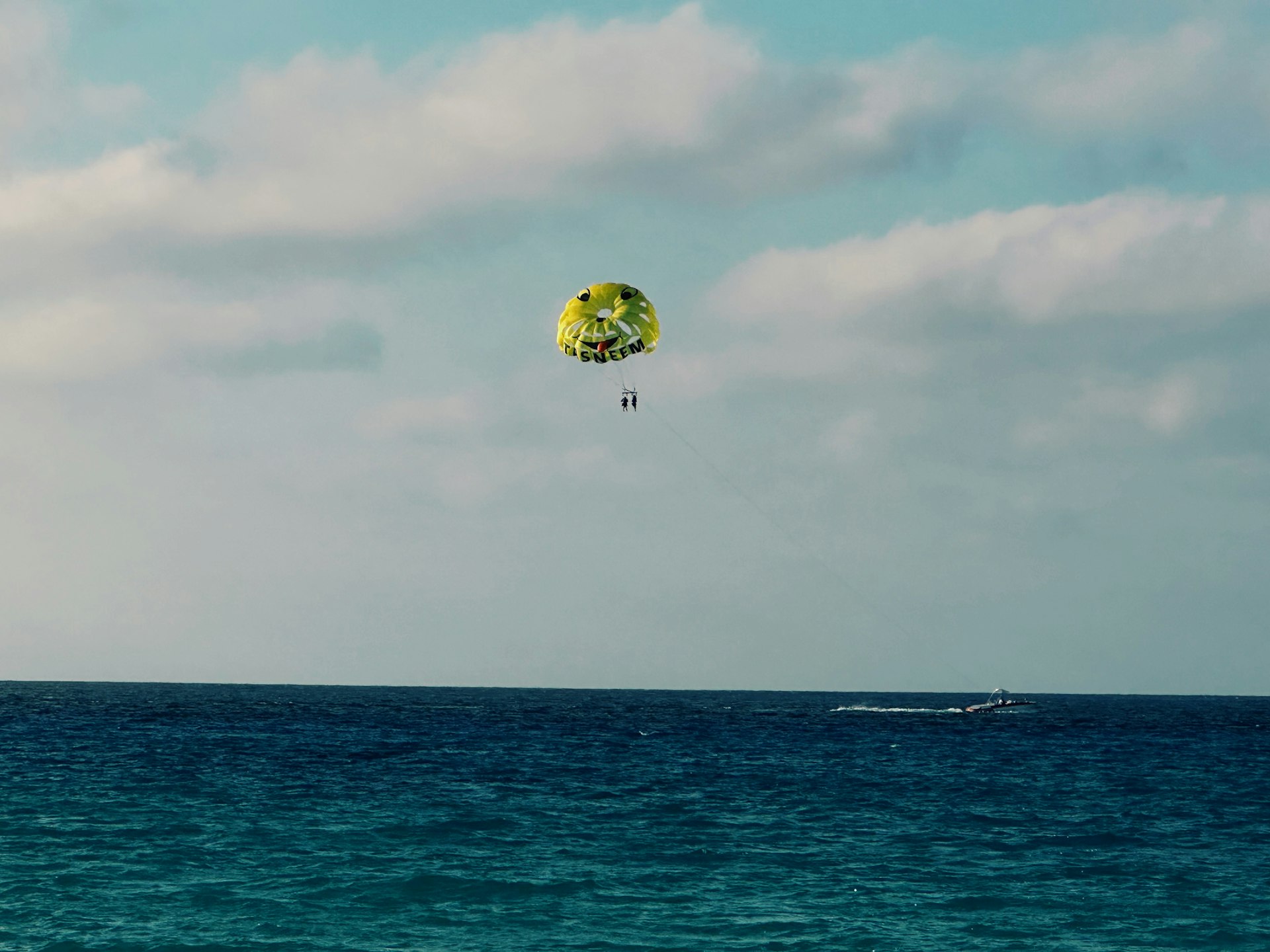 Person parasailing over the blue ocean with clouds.
