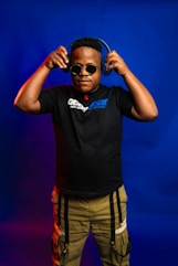 Man wearing headphones and sunglasses against blue background.