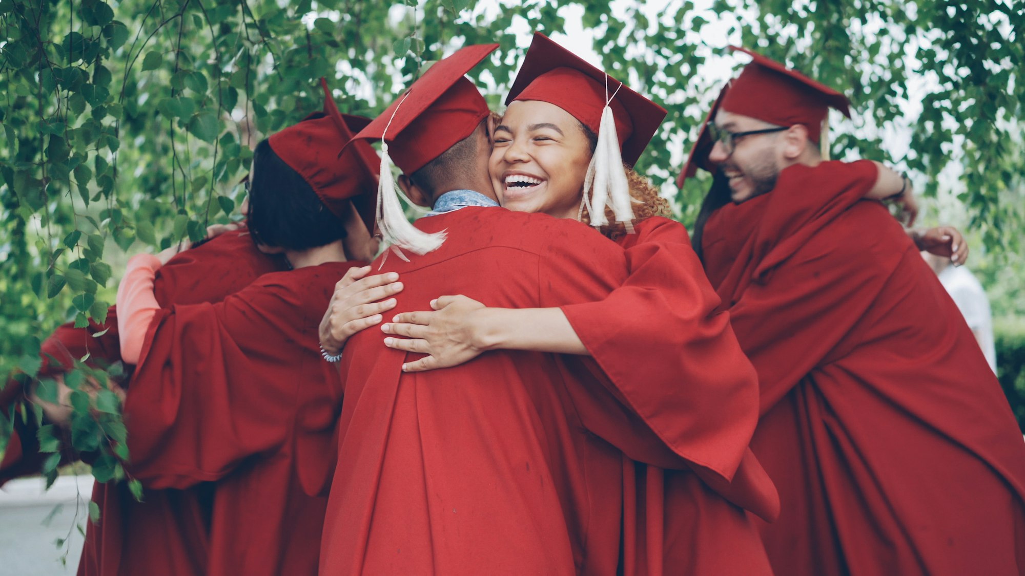 Graduates in red robes hugging each other in celebration outdoors