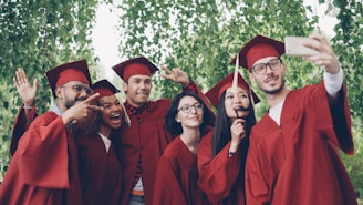Graduates in red gowns taking a selfie outdoors.