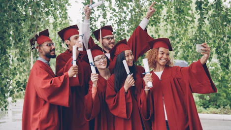 Graduates in red robes taking a selfie with diplomas