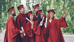 Graduates in red gowns take a selfie with diplomas.