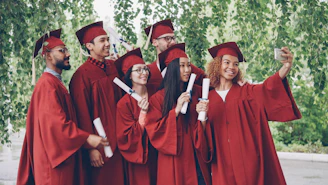 Graduates in red gowns take a selfie with diplomas.