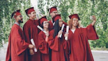 Graduates in red gowns take a selfie with diplomas.