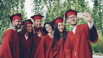 Graduates in red gowns taking a selfie outdoors.