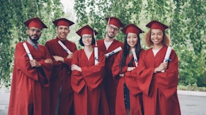 Six graduates in red gowns holding diplomas