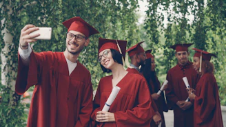 Graduates in red robes taking a selfie with diplomas.