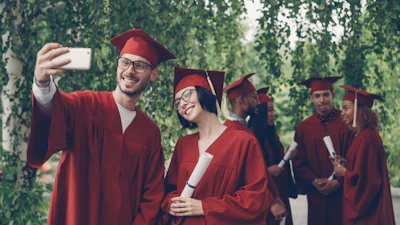 Graduates in red robes taking a selfie with diplomas.