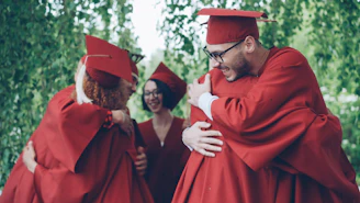 Graduates in red gowns hug each other happily.
