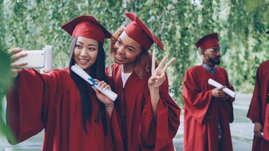 Graduates in red gowns take a selfie with diplomas.