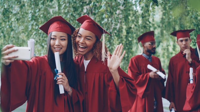Graduates in caps and gowns taking a selfie outdoors.