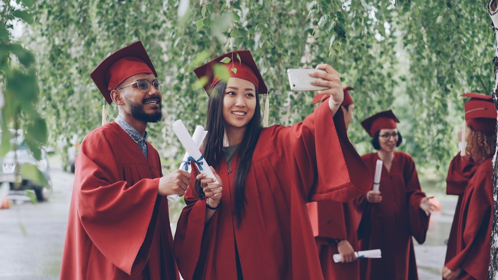 Graduates in red gowns taking a selfie with diplomas