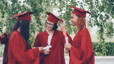 Three graduates in red gowns holding diplomas