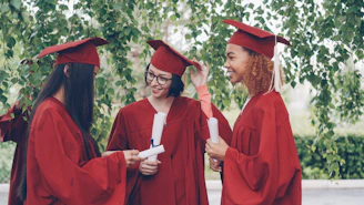 Three graduates in red gowns holding diplomas