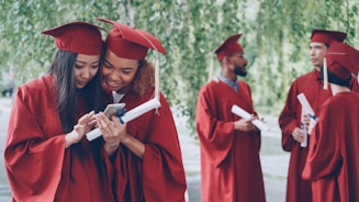 Graduates in red gowns look at a phone together.